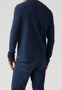 Marineblaues, langärmeliges, geripptes Shirt mit Rundhalsausschnitt, kombiniert mit dunklen Denim-Jeans, die dezente Nähte und Gesäßtaschen aufweisen.