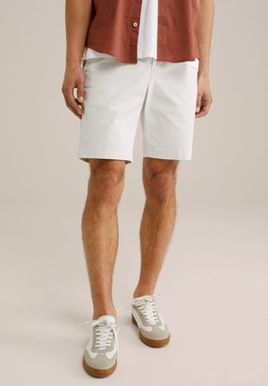 White cotton shorts with a straight cut, paired with light grey and white sneakers featuring a brown sole and white laces.