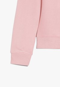 Jasnoróżowy rękaw bluzy z ribbowanym mankietem; miękka faktura, gładkie wykończenie i ustrukturyzowany krój. Brak wzorów lub widocznych detali metalowych.