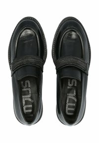 Chaussures en cuir noir avec une finition lisse et un large élastique sur le dessus. Elles présentent un bout arrondi et des coutures décoratives.