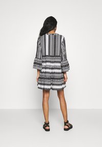 Svart- och vitmönstrad klänning med trumpetärmar, volang i nederkant och geometriska mönster, tillverkad i lättviktig tyg. Stylad med svarta sandaler.