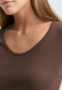 Braunes geripptes Tanktop mit Rundhalsausschnitt. Der Stoff wirkt weich mit einer glatten Textur und subtilen Glanz. Nahaufnahme des Kragens.