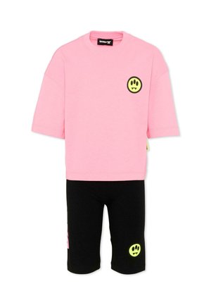 Camisetta rosa a maniche corte con logo faccina sorridente gialla e pantaloncini neri fino al ginocchio con design abbinato della faccina sorridente gialla.