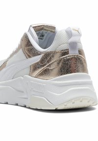 Weißer Sneaker mit metallisch goldenen Akzenten, strukturiertem Mesh und glatten Lederabschnitten, ausgestattet mit einer dicken Sohle und einem markanten Fersenbereich.