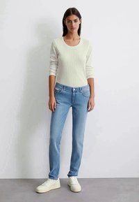 Gai pelēks ribots garām piedurknēm tops ar apaļu kakla izgriezumu, saskaņots ar vidējiem zilajiem džinsiem un baltām kedām uz neitrāla fona.