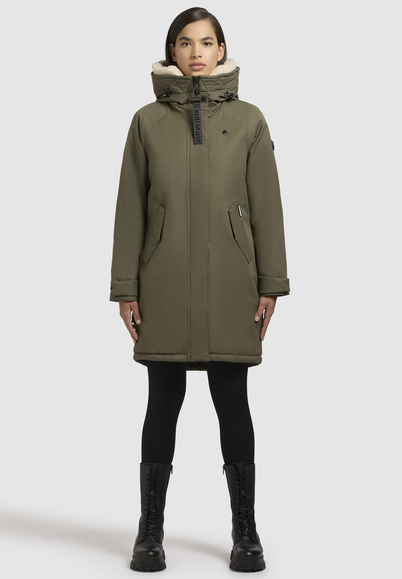 Cappotto imbottito verde oliva con chiusura a zip, ampio cappuccio e foderato in pile. Presenta due tasche laterali e polsini regolabili.