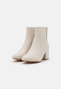 Beżowe skórzane botki za kostkę o gładkim wykończeniu, z wysmuklonym noskiem i obcasem w kształcie bloku. Posiadają elastyczne boczne panele ułatwiające zakładanie.