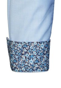 Helle blaue Stoffhose mit einem floral gemusterten Saum in Marineblau, der kleine blaue und weiße Blumen zeigt, glatte Textur.