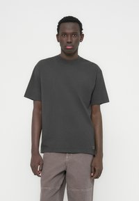 Μαύρο γκρι βαμβακερό T-shirt με στρογγυλή λαιμόκοψη και κοντά μανίκια, με άνετη εφαρμογή, σε συνδυασμό με ανοιχτό καφέ παντελόνι.