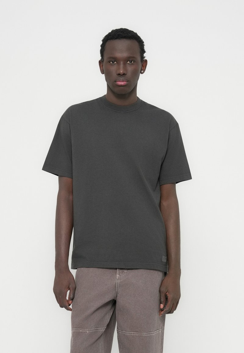 Μαύρο γκρι βαμβακερό T-shirt με στρογγυλή λαιμόκοψη και κοντά μανίκια, με άνετη εφαρμογή, σε συνδυασμό με ανοιχτό καφέ παντελόνι.