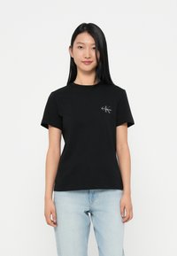 Μαύρο βαμβακερό T-shirt με στρογγυλή λαιμόκοψη, κοντά μανίκια και μικρό λευκό λογότυπο στο αριστερό στήθος. Απλός σχεδιασμός, άνετη εφαρμογή.