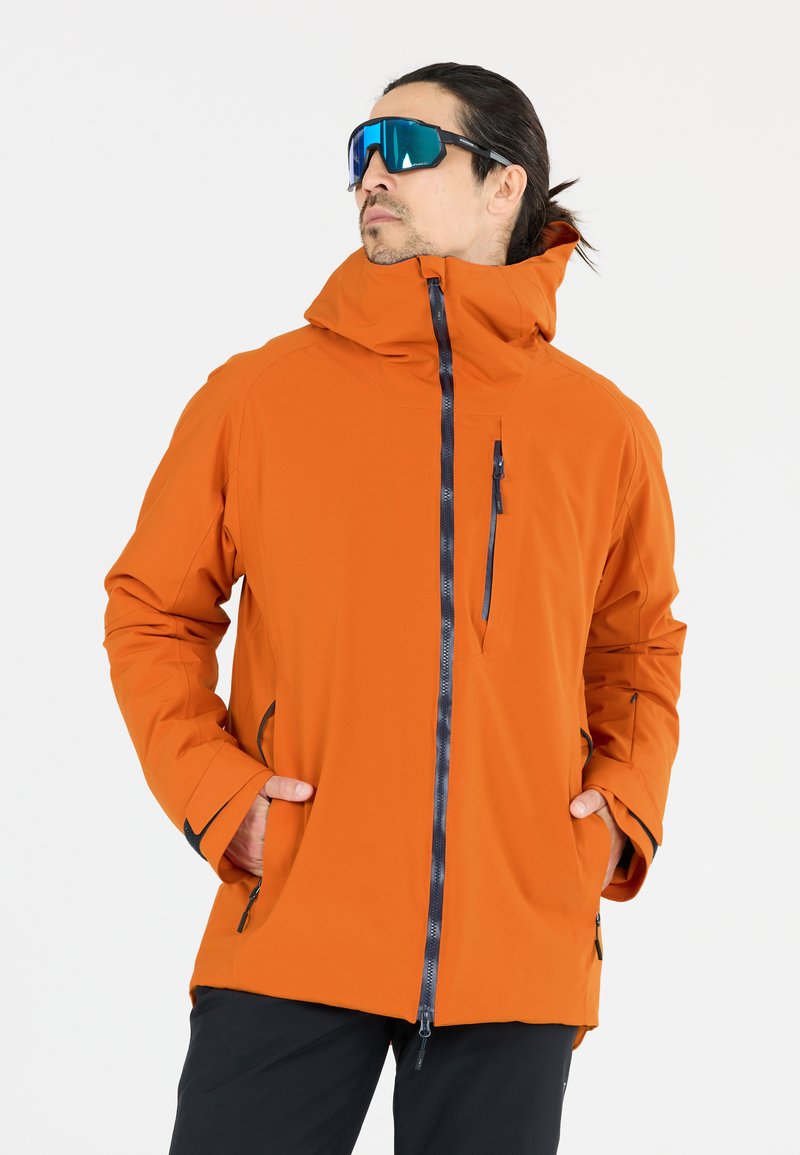 Orange vandtæt jakke med høj krave, frontlynlås, sidelommer og kontrasterende sorte detaljer. Glat, holdbart stof; afslappet pasform.