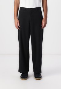 Black, wide-leg trousers with a button closure and belt loops, made from a smooth fabric. Worn with a white shirt and black sneakers.