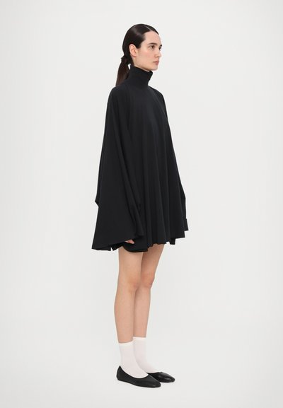 Mustat ylisuuret turtleneck-mekot, joissa on leveät hihat; sileä kangas; polvipituinen; yhdistetty valkoisiin nilkkasukkiin ja mustiin ballerinoihin.