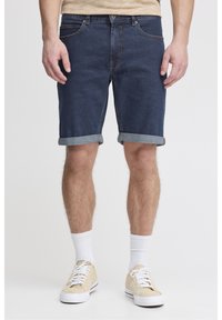 Tummansiniset denimshortsit, joissa on käännetyt lahkeet, viisi taskua ja kontrastiväriset tikkausompeleet. Yhdistetty beigenvärisiin lenkkareihin ja valkoisiin keskipitkiin sukkiin.