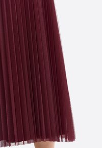 Burgundy pleated skirt made of sheer fabric, featuring vertical pleats that create a textured appearance and a flowing silhouette.