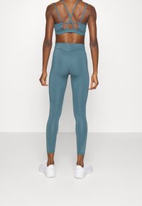 Sujetador deportivo en azul verdoso con tirantes cruzados y leggings de talle alto a juego. Ambos están hechos de un material suave y elástico, con un diseño sin costuras.