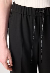 Zwarte sportbroek met een elastische tailleband, voorzien van een trekkoord met merktekst, zijzakken en een gestructureerde stofafwerking.