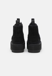 Botas de tobillo negras de ante con una plataforma gruesa, punta redondeada, tiradores y forro de piel sintética en la parte superior.