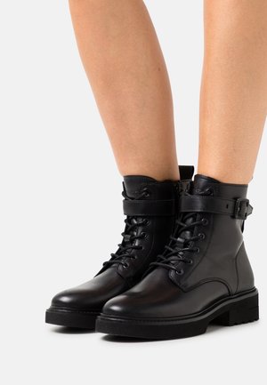 Zwarte leren enkellaarsjes met een ronde neus, veters aan de voorkant, een enkelbandje en een gerubberde zool met textuur. Voorzien van minimalistische metalen accenten.