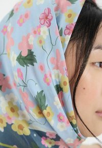 Écharpe florale avec un fond bleu clair, ornée de fleurs roses et jaunes, texture douce, drapée élégamment autour du visage.