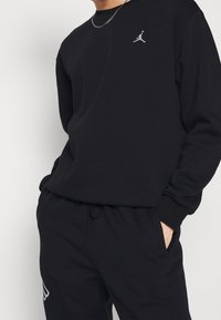 Sudadera negra con cuello redondo, puños acanalados y un pequeño logo Jumpman blanco. Combinada con pantalones joggers negros con un detalle blanco.