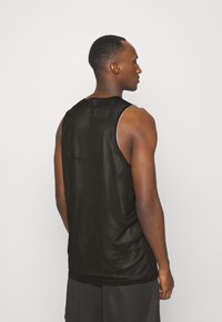 Musta verkkoneule sleeveless urheilutoppi, jossa on pyöreä kaula-aukko, löysä istuvuus ja hienovarainen tekstuuri, valkoisilla yksityiskohdilla käsivarsia ympärillä.