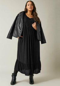 Vestido largo negro con un dobladillo con volantes, tela texturizada y cuerpo bordado. Combinado con una chaqueta de cuero ajustada y botas de tobillo.