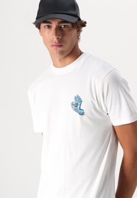 Hvid bomulds T-shirt med et blåt grafisk print af en skrigende hånd på venstre bryst. Stoffet er glat, og pasformen er casual.