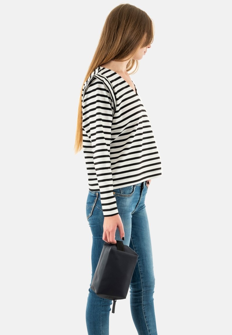 Camiseta de manga larga a rayas en blanco y negro, combinada con unos vaqueros ajustados azules. El modelo sostiene un pequeño bolso negro con un asa.