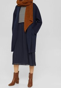 Lång marinblå rock, randig topp, plisserad marinblå kjol och bruna läderankelboots. Scarf i bränd orange, med en texturerad, mjuk yta.