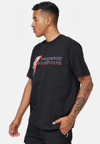 Svart bomullströja med en framgrafik av David Bowies Aladdin Sane omslagskonst. Kort ärmar och rundad hals.