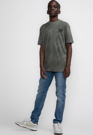Donkergroen t-shirt met korte mouwen en een subtiel textuurpatroon, gecombineerd met lichtblauwe slim-fit jeans en grijze sneakers met gouden accenten.