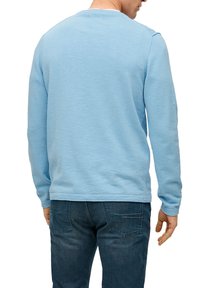 Man wearing a light blue long-sleeve shirt and dark blue jeans, shown from the back against a white background.