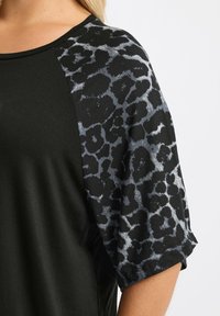 Schwarzes Oberteil mit kurzen Ärmeln, das ein graues Leopardenmuster zeigt. Glattes Material mit Rundhalsausschnitt und kontrastierenden Ärmeln.