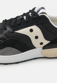 Fekete és szürke sneaker, texturált velúrból és szövetből készült felsőrésszel, fehér logó akcentussal és fekete fűzőkkel, fehér gumi talpon.