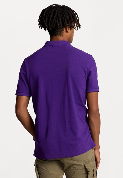 Polo shirt violet à manches courtes, avec un col classique et un tissu texturé. Porte avec un short cargo de couleur claire.