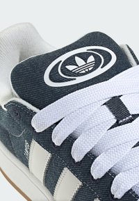 Tennarit denim-materiaalista tummansinisellä yläosalla, valkoisilla nauhoilla ja kolmella valkoisella raidalla. Sisältää logon kielessä ja tekstuuripinta.