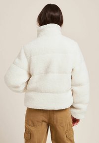 Chaqueta blanca y esponjosa con costuras acolchadas, cuello alto y puños elásticos. Presenta una superficie texturizada y un ajuste cómodo.