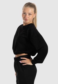 Schwarzer, kurz geschnittener Sweatshirt und passende Hose, aus weichem Stoff mit elastischem Bund. Der Sweatshirt hat einen runden Halsausschnitt und einen entspannten Schnitt.
