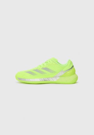 Pantof sport de culoare verde lime, cu un superior din plasă, trei dungi argintii pe lateral și o talpă texturată concepută pentru aderență și suport.