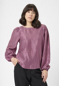 Lila strukturierte Bluse mit langen Puffärmeln, rundem Ausschnitt und elastischen Bündchen. Kombiniert mit schwarzen Hosen. Glattes, glänzendes Material.