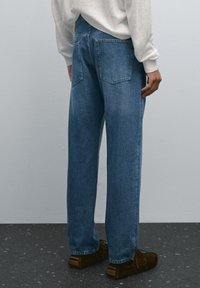 Jeans in denim azzurro chiaro con taglio dritto, dotati di due tasche posteriori, leggera scoloritura e vestibilità rilassata. Indossati con scarpe marroni.