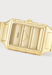 Goldfarbene Edelstahl-Uhr mit rechteckigem Zifferblatt, strukturierten Akzenten und glänzender Oberfläche. Markenname "FOSSIL" auf dem Ziffernblatt angezeigt.