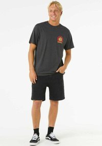 Gray cotton t-shirt featuring a colorful lion logo on the chest, paired with black denim shorts and black sneakers. Simple design.