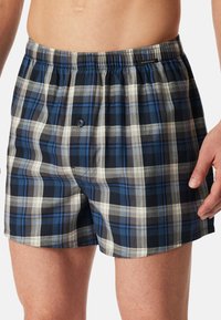 Boxershorts van katoen in een blauw, grijs en wit geruit patroon. Voorzien van een elastische waistband en een enkele knoopsluiting.