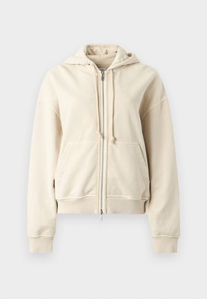 Μπεζ φούτερ με φερμουάρ και κορδόνια, με μπροστινές τσέπες τύπου πουγκί, ριμπ μανσέτες και τελείωμα, παρουσιάζεται σε απλό ανοιχτό γκρι φόντο.