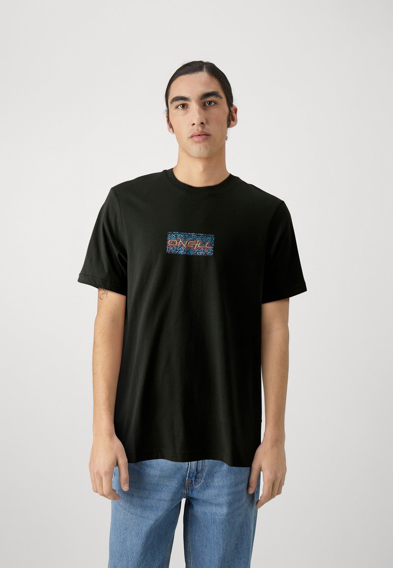 Camiseta de algodón negra con un gráfico colorido en el centro. Manga corta, cuello redondo y un ajuste holgado. Llevada con jeans de color azul claro.