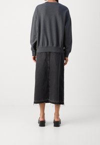 Grijze oversized sweatshirt gecombineerd met een zwarte denim rok, met een rafelige zoom en voorzakken. Schoeisel: zwarte platform sandalen.