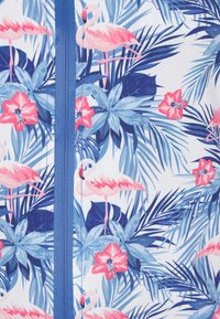 Tropisk mönstrad tyg med rosa flamingos, röda blommor och gröna blad på en vit bakgrund, med en blå dragkedja i mitten.